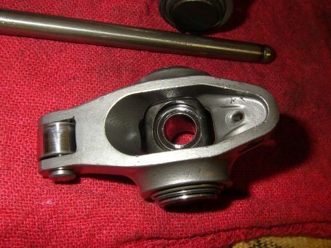 1990 Ford Bronco - Close-up of a single full roller rocker arm laid on a red shop rag, showing the roller tip, needle-bearing trunnion bore and threaded stud…