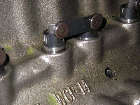 1990 Ford Bronco - Extreme close-up of a bare aluminum engine block's lifter valley, showing a hydraulic roller lifter pair retained by a steel guide link bar…
