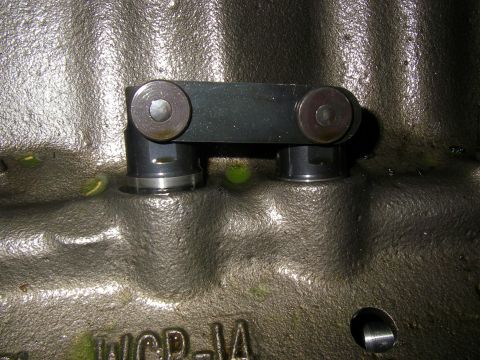 1990 Ford Bronco - A link-bar roller lifter pair installed in two adjacent lifter bores of a bare cast-iron engine block, photographed straight on so the tie…