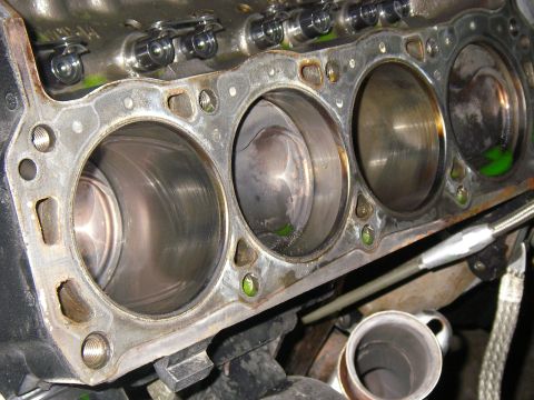 1990 Ford Bronco - Close-up of an engine block deck with the cylinder head removed, showing one bank of four cylinder bores with the pistons at the tops and a…