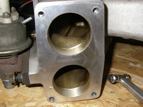 1990 Ford Bronco - Close-up of a twin-bore aluminum throttle body with the mounting flange facing the camera, showing both bores freshly ported and smoothed w…