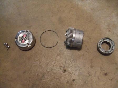 1996 Ford Bronco - Various parts of a hubcap are laid out on a concrete surface, including screws and a bearing, with a Supermotors logo at the bottom right.