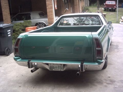 1977 Ford Ranchero - Rear view of a green 1977 Ford Ranchero. A red pickup truck is visible in the background.
