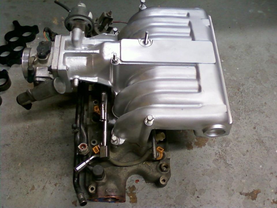 Polished aluminum upper intake manifold with throttle body on a garage floor