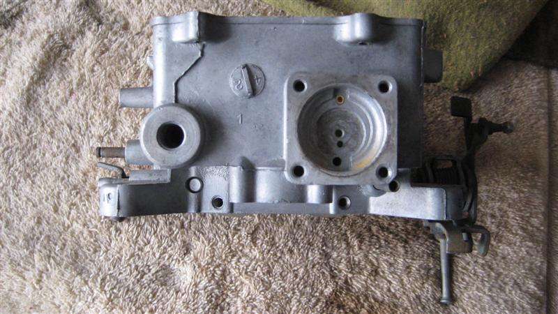 Gray metal carburetor with visible casting marks and linkage on a textured surface