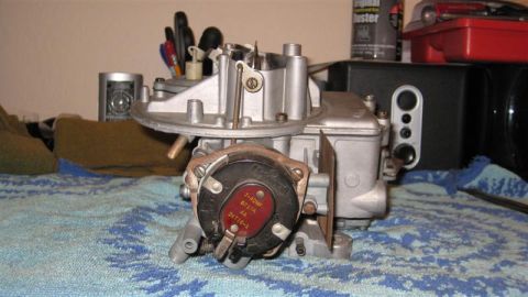 1968 Ford Ranchero - A carburetor sits on a patterned cloth, with various items in the background including pens and a red toolbox.