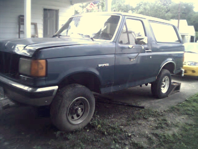 Dark blue Ford Bronco, front quarter view, hood slightly ajar, on a gravel driveway