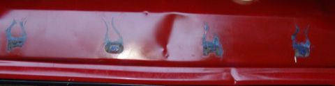 1978 Ford Bronco - Close-up of a red sheet-metal body panel showing a crease dent and four small ground-down repair spots with bluish weld or filler discolora…