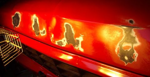 1978 Ford Bronco - Rust damage is visible on the hood of a red vehicle, indicating areas where paint has failed.