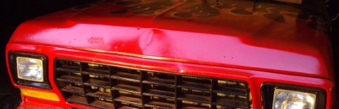 1978 Ford Bronco - Night front-end close-up of a red Ford truck showing the egg-crate grille, rectangular sealed-beam headlights and amber turn signals, with…