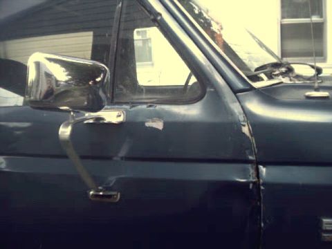1989 Ford Bronco - Close-up of a truck's door and side mirror, showing some wear and tear on the paint.