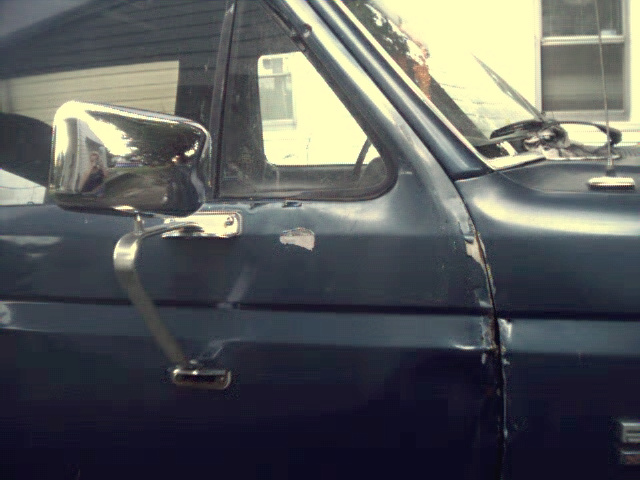 Side view of a dark blue pickup truck door with a chrome mirror. Some paint chips are visible