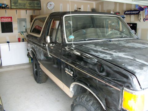 1990 Ford Bronco - This Ford Bronco is parked in a garage with various items on the shelves in the background.