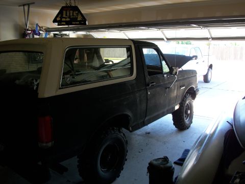 1990 Ford Bronco - A dark-colored Ford Bronco sits in a garage with its hood up, next to another white vehicle.