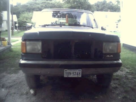 1989 Ford Bronco - Frontal view of a dark SUV with a missing grille and visible 4x4 badging.