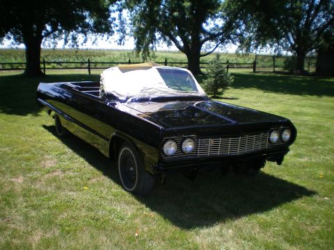 1964 Chevrolet Impala - A black 1964 Chevrolet Impala convertible is parked on a grassy lawn with trees in the background.