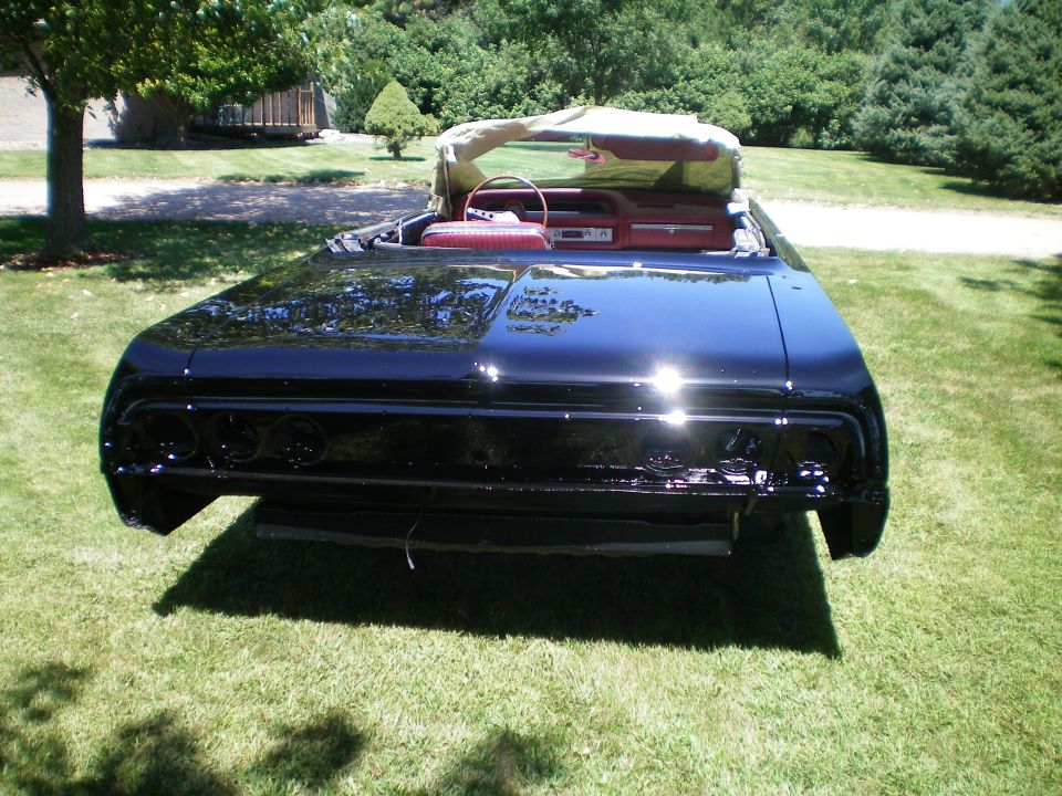 Rear of gloss black 1960s convertible on grass, taillight lenses and bumper removed