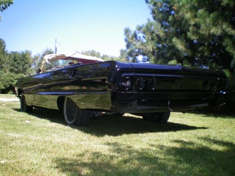 1964 Chevrolet Impala - A black 1964 Chevrolet Impala convertible is parked on a grassy lawn with trees in the background.