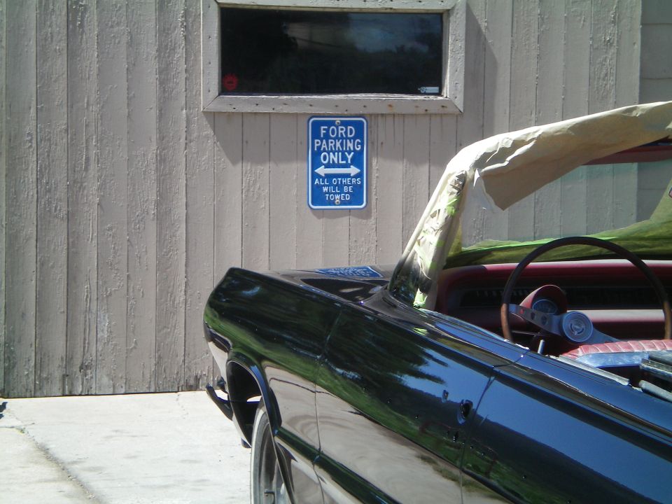 Black convertible with red interior, masked for paint, parked below a Ford Parking Only sign