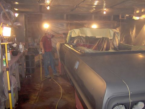 1964 Chevrolet Impala - A car is being painted in a workshop, with a person working on it and protective coverings in place.