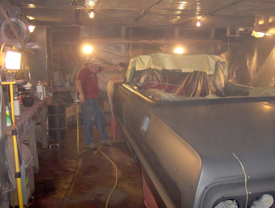 Car body covered in plastic sheeting, being prepped for paint in a workshop with lights and equipment