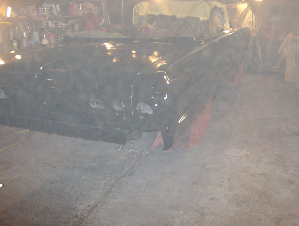 Car body on jack stands in a garage, covered in dust. The front end has four headlights