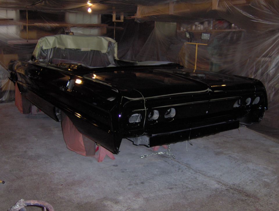 Rear view of a black 1964 Chevrolet Impala convertible being worked on in a garage