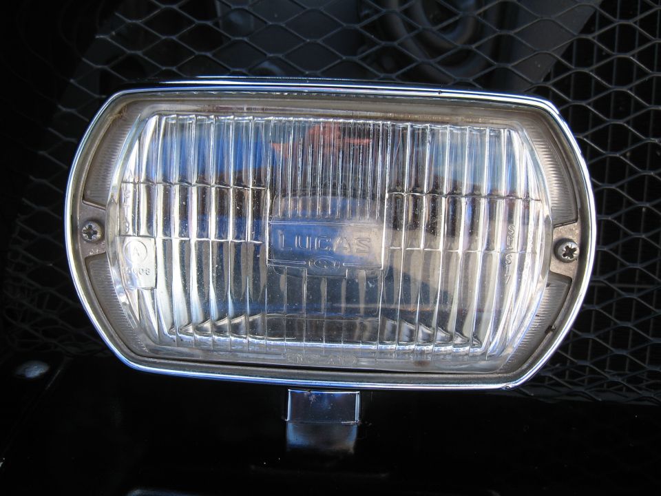 Close-up of a Lucas headlight with a chrome bezel and a black grille behind it