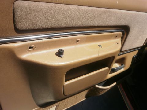 1991 Ford Bronco - Close-up of a tan interior door panel, showing chrome trim and a missing knob, with a storage compartment below.