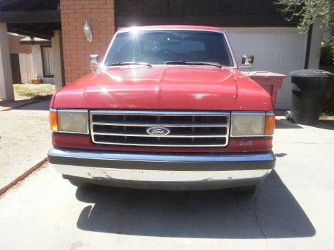 1991 Ford Bronco - A red Ford pickup truck is parked in front of a garage. The 4x4 badging is visible on the front fender.