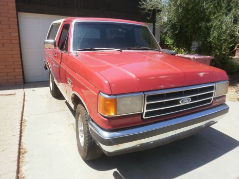 1991 Ford Bronco - This red Ford Bronco is parked in front of a garage with a white door.