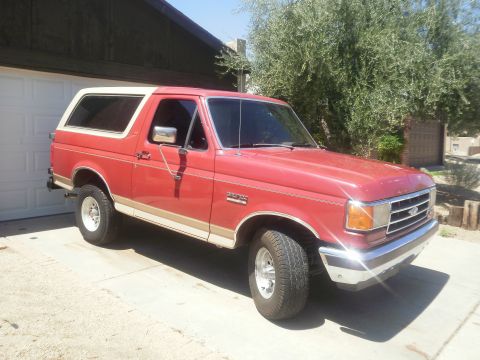 1991 Ford Bronco - A red 1991 Ford Bronco with a tan stripe and white top is parked in a driveway.