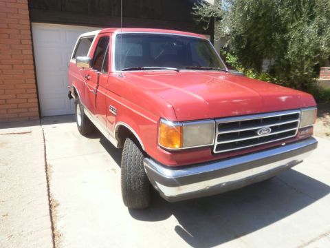 1991 Ford Bronco - This red Ford Bronco is parked in front of a garage on a sunny day.