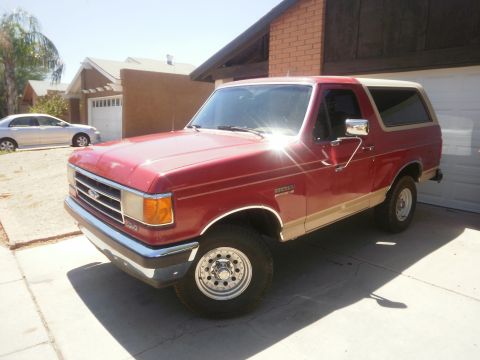 1991 Ford Bronco - A red and tan 1991 Ford Bronco is parked in front of a garage and house.