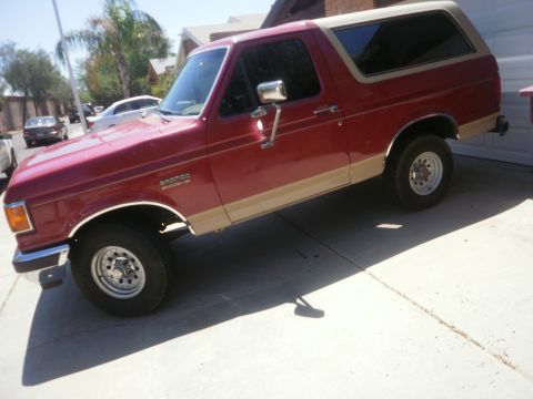 1991 Ford Bronco - This red and tan 1991 Ford Bronco is parked in a driveway on a sunny day.