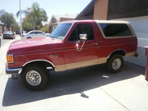 1991 Ford Bronco - Side view of a red 1991 Ford Bronco with tan trim parked in a driveway.
