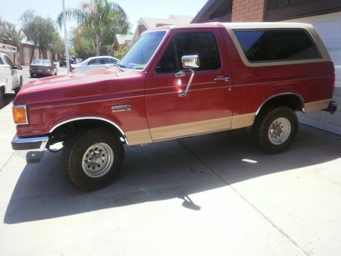 1991 Ford Bronco - Side view of a two-tone red and tan Ford Bronco parked on a concrete driveway.