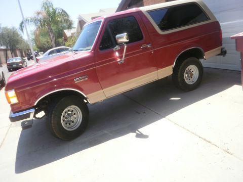 1991 Ford Bronco - This red and tan 1991 Ford Bronco is parked in a driveway, showing its front three-quarter view.