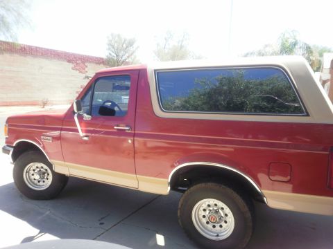1991 Ford Bronco - This two-tone red and tan Ford Bronco is shown from the side under a bright sky.