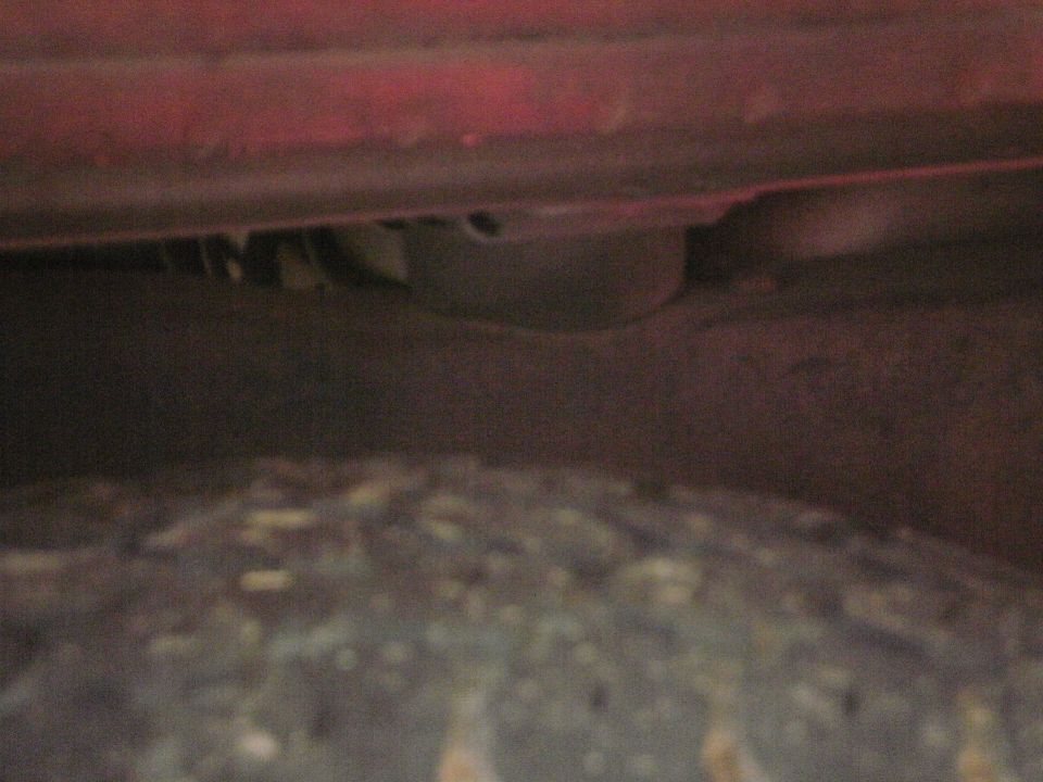 Rusted-through inner fender lip inside the wheel well of a red vehicle above a muddy tire