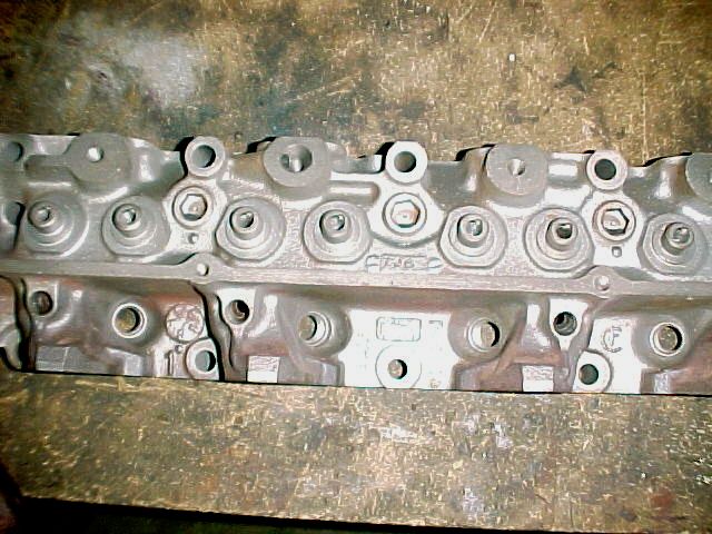Close-up of bare cast-iron V8 cylinder head deck with casting marks on wood bench