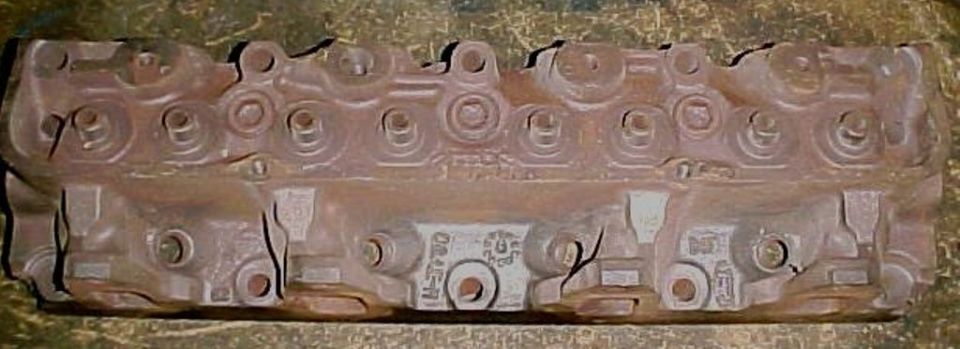 Rusty bare cast-iron V8 cylinder head from above showing rocker pedestals and casting marks