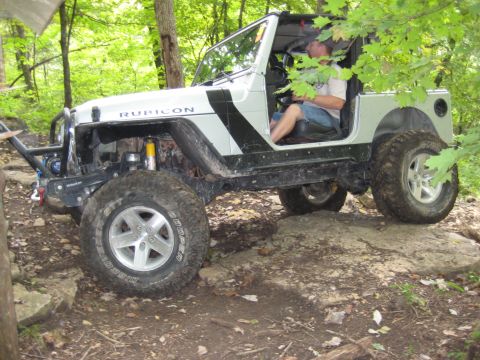 2005 Jeep Wrangler - A driver navigates a silver Jeep Wrangler Rubicon over rocky terrain in a wooded area.
