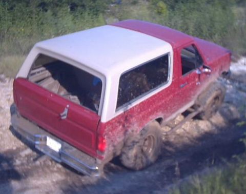 1989 Ford Bronco - This red and white SUV is covered in mud, suggesting off-road use.