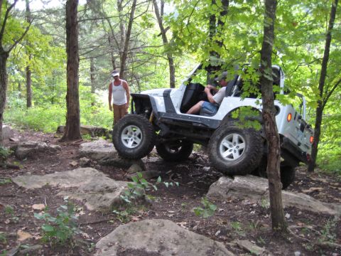 2005 Jeep Wrangler - A white 2005 Jeep Wrangler TJ Rubicon navigates a rocky trail with a person driving and another standing nearby.