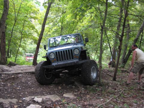 2005 Jeep Wrangler - Light blue-gray Jeep Wrangler with the top removed climbing a rocky descent on a wooded trail, front suspension flexed with oversized mud-t…