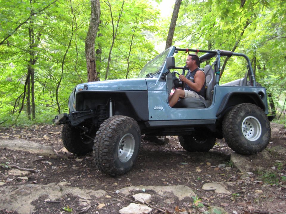 Blue 2005 Jeep Wrangler TJ with aftermarket wheels and tires on a rocky trail