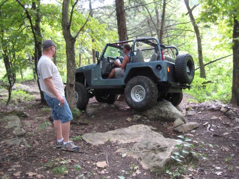 2005 Jeep Wrangler - A Jeep Wrangler navigates a rocky off-road trail surrounded by trees.