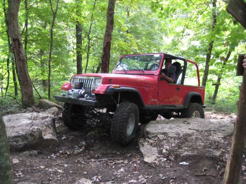 2005 Jeep Wrangler - A red Jeep Wrangler navigates a challenging rocky trail in a wooded area.