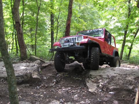2005 Jeep Wrangler - Red Jeep Wrangler navigating a challenging rocky trail through a wooded area.